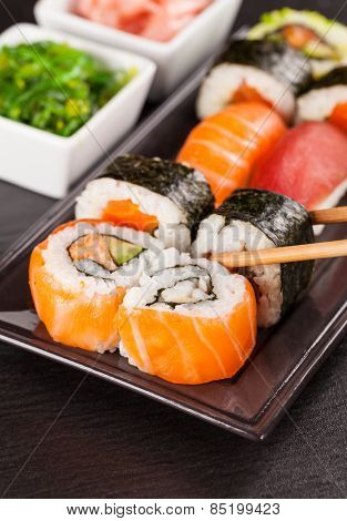 Delicious sushi rolls served on black plate and stone