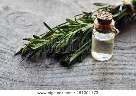Rosemary essential oil in a glass bottle with fresh green rosemary herb on old wooden table. Rosemary oil for spa, aromatherapy and body care. Extract oil of rosemary. Selective focus.