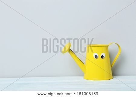 Yellow Watering Can With Googly Eyes On A Grey Background
