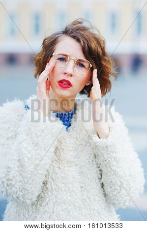 Young Beautiful Girl Student In A White Jacket In The Town Square With Narrowed Eyes Looking Through