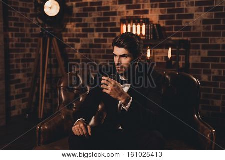 Handsome Young Man In Elegant Suit With Glass Of Whiskey Relaxing On Sofa