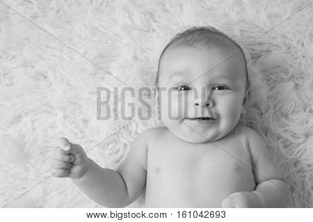 A black and white portrait of a baby boy lying on on a flokati rug. He is smiling and looking at the camera