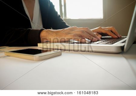 Asian business woman manager analyzing datum in charts and typing on computer making notes in documents on the table in office vintage color selective focus. Business concept.