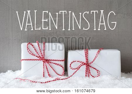 German Text Valentinstag Means Valentines Day. Two White Christmas Gifts Or Presents On Snow. Cement Wall As Background. Modern And Urban Style.