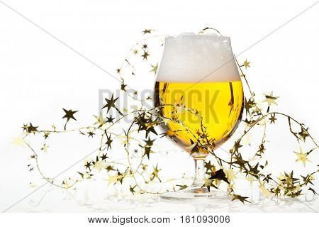 Full snifter glass of pale lager of pilsner beer with a large head of foam and golden christmas tinsel on white background