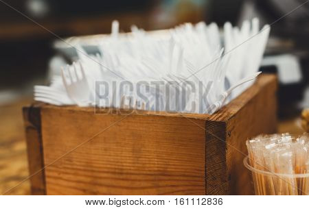 Set of plastic disposable cutlery, forks and knives and individual packed toothpicks in wooden box. Catering utencils for bistro fast food cafe on country fair, detail closeup