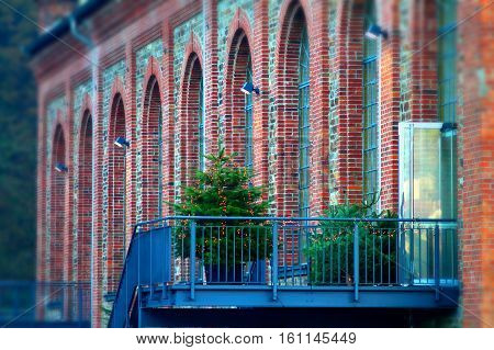 Cone-bearing evergreen tree with lights on forged iron balcony against brick wall building. Christmas bazaar in Bad Ems, germany.