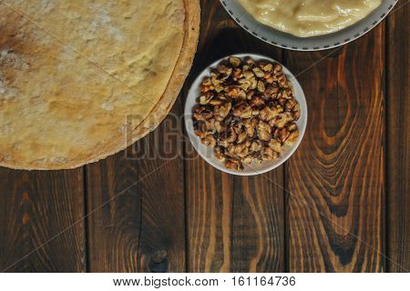 Ingredients for baking a cake, top view on wooden board. shortcakes, buttercream or cream and nuts on a plate on vintage wooden kitchen table. copyspace for cook recipe.