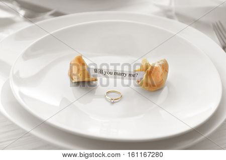 Offer of marriage with fortune cookie and ring on white plate closeup