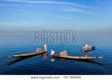 Myanmar travel attraction landmark - Traditional Burmese fishermen with fishing nets on boats at Inle lake in Myanmar famous for their distinctive one legged rowing style