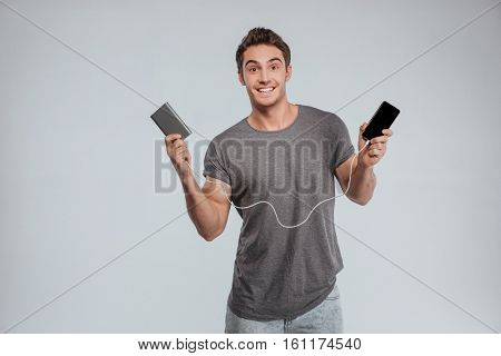 Smiling casual man charging his mobile phone isolated on the white background