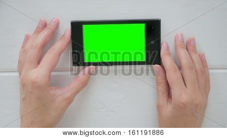 Woman using horizontal smartphone with green screen. Close up shot of woman's hands with mobile Close up shot of woman's hands with mobile White wooden background