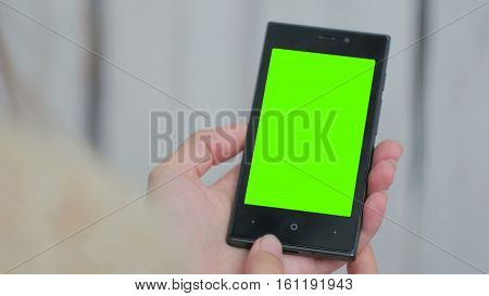 Woman looking at vertical smartphone with green screen. Close up shot of woman's hands with mobile. White wooden background