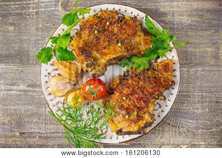 Fried meat on a plate with tomatoes and herbs peppers. The food on the wooden table gray background.