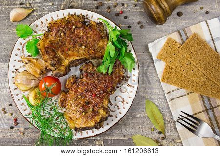 Fried meat on a plate with tomatoes and herbs peppers. The food on the wooden table gray background.