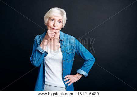 Mull it over. Pleasant thoughtful woman holdign her hand on the chin and thiking while standing isolated on black background