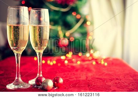 Two glasses of champagne near beautiful christmas tree. Pouring champagne into glass. Merry Christmas and Happy New Year. Moody style. Selective focus.