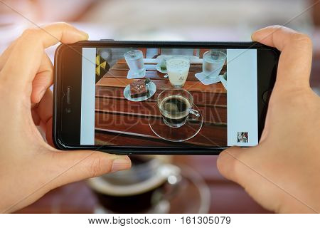 Smartphone in hand with coffee and cake on table.Photo coffee and cake on diaplay.