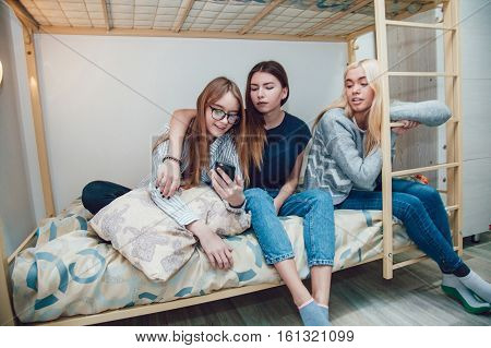 Beautiful girls sitting on a bed in hostel talk and using smartphone.