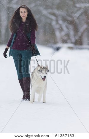 Human and Pet Relationships Ideas and Concepts.Lovely Caucasian Brunette Woman Along With Her Husky Dog Walking Outdoors in Winter Forest. Vertical Image Orientation
