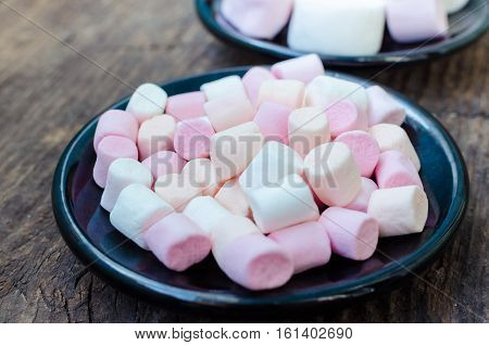 Colorful mini marshmallows in a black plates on a wooden background. Different mini white pink and orange puffy marshmallows. Marshmallow concept.