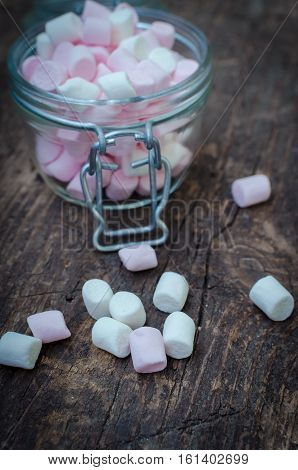 Pink and white mini marshmallows in a jar on an old rustic wooden table with space for text. Mini white and pink puffy marshmallows. Marshmallow concept. Copy space. Selective focus.