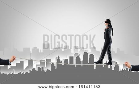 Businessman with blindfolder on eyes walking on rope