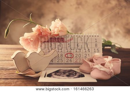 Calendar with mark, ultrasound picture of baby and children shoes on table