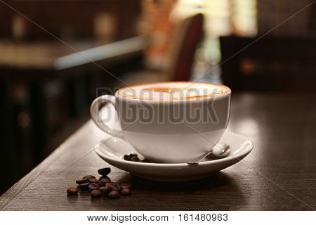 Cup with hot tasty coffee on wooden table in cafe, close up view