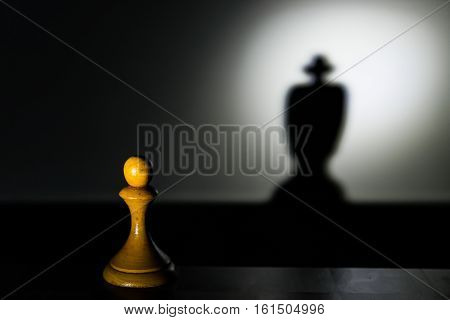 a chess pawn casting a king piece shadow in dark concept of strength and aspirations