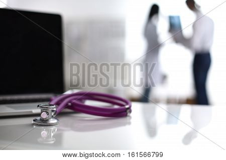 Laptop and stethoscope on the desk , doctors standing in the background.