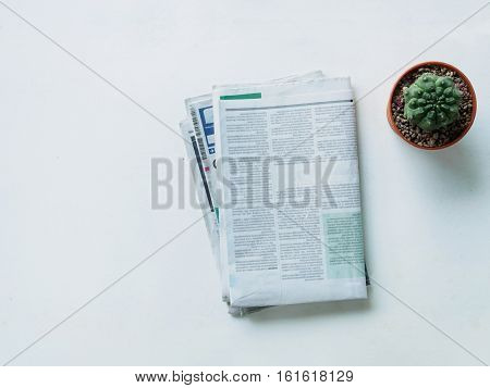 Top view stack newspaper and cactus on white dask with copy space