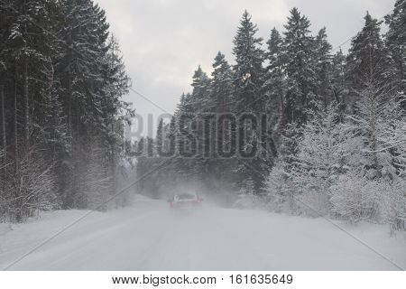 Red car driving on a snowy road in the woods in a snow storm