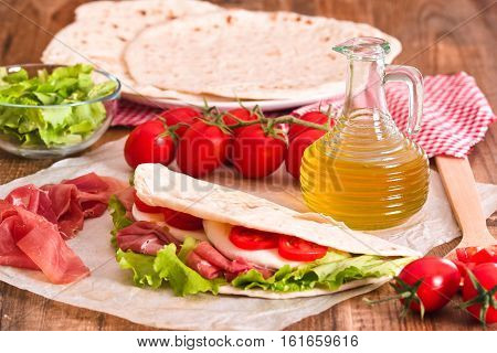 Piadina with ham and lettuce on baking paper.