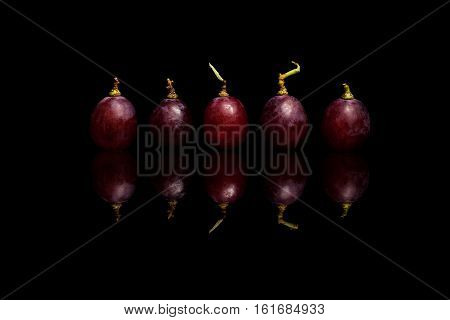 Five rred grapes isolated on black reflective background