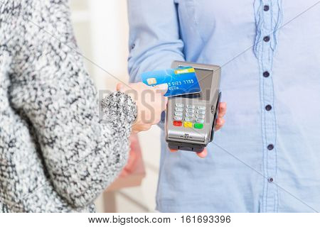 Hand holding contactless credit or debit card over wireless payment terminal at shop