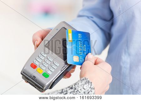 Hand holding contactless credit or debit card over wireless payment terminal at shop