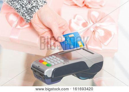 Hand holding contactless credit or debit card over wireless payment terminal at shop with gifts in the background 