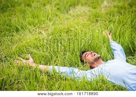 Happy pretty man lying on the green grass with arms outstretched