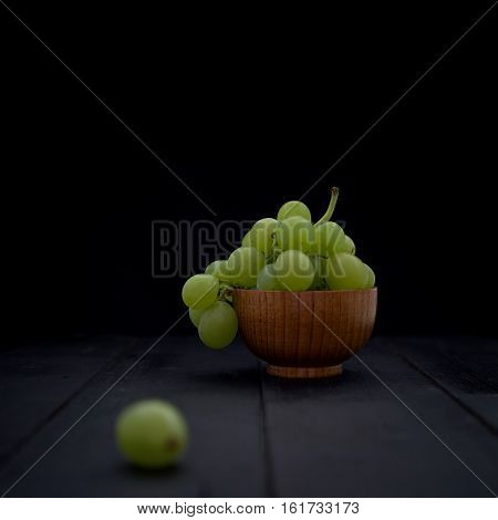 Organic white grapes in brown wood bowl on black wood boards. Selective focus on the grapes in bowl. Square crop.