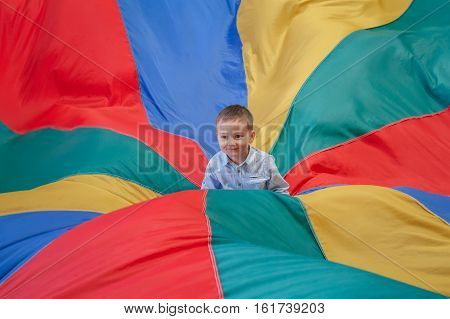 Portrait of white Caucasian child boy toddler sitting in the center of playground rainbow parachute celebrating his birthday at party