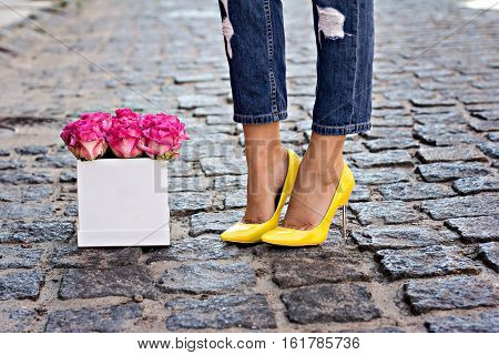 The bouquet of pink roses and female legs in jeans and yellow shoes with heels.