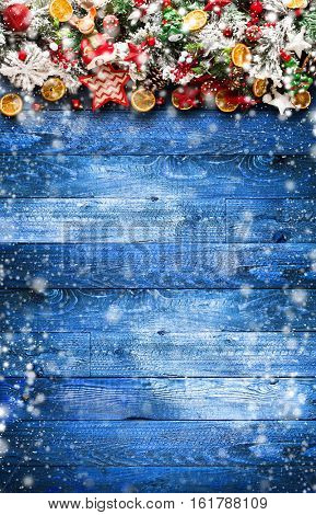 Merry Christmas Frame with Snow and wood green pine, colorful baubles, knots with berries,stars, orangesand other seasonal stuff over an old wooden aged background