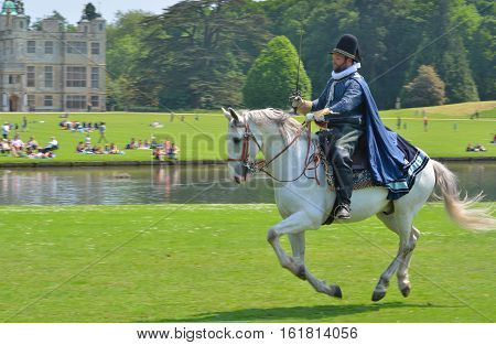 SAFFRON WALDEN, ESSEX, ENGLAND - JUNE 05, 2016: Man in Elizabethan costume with sword on a horse galloping  in front of stately home.