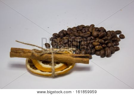 Hill, flavored, roasted coffee and cinnamon with dried orange on a white background, focus on coffee beans