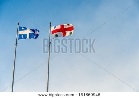 Montreal and Quebec flags waving over blue sky