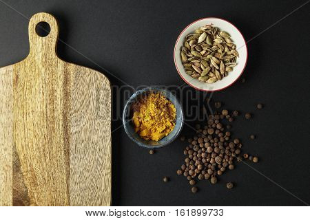 Cutting board with bowls with tumeric cardamom on black background. Space for text