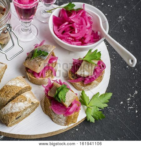 Small sandwiches for aperitif with marinated sweet onion and salt herring with greens on a dark background. Finger food appetizer. Top view.
