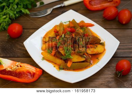 Stew with potatoes, carrots, pickles, tomatoes and hot peppers. Azu by Tartarian on a white square plate. Wooden rustic background. Top view