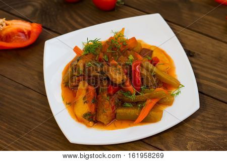 Stew with potatoes, carrots, pickles, tomatoes and hot peppers. Azu by Tartarian on a white square plate. Wooden rustic background. Top view